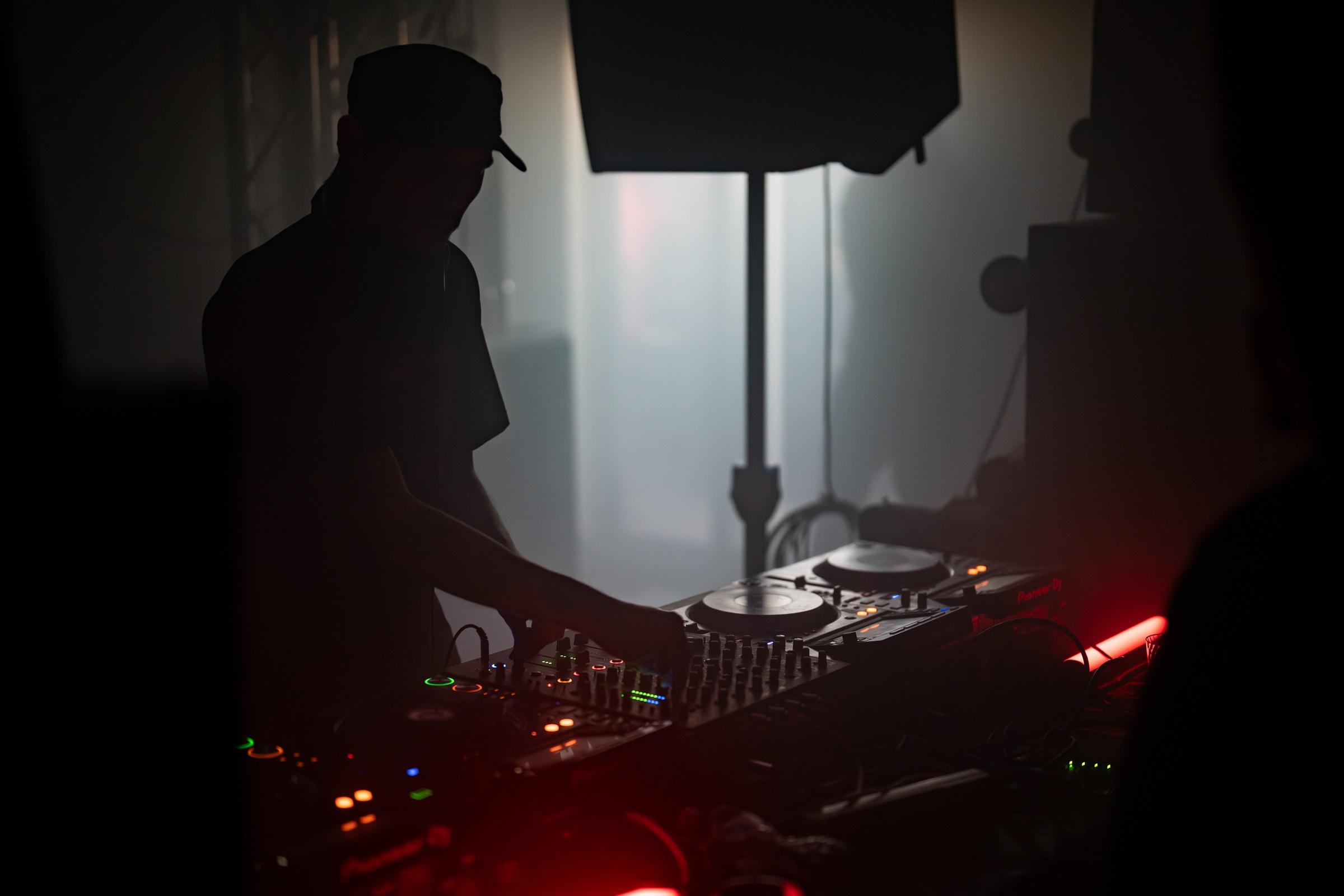 DJ in a cap at the decks, red light from below